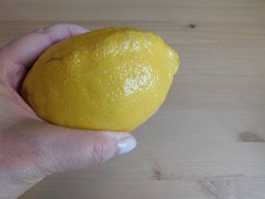 Gri desenli arka planda izole edilmiş, olgun sarı bir limonu tutan bir kadın. Yakın plan, sağlıklı yiyecek kavramı.