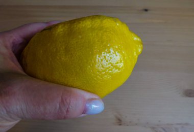 Gri desenli arka planda izole edilmiş, olgun sarı bir limonu tutan bir kadın. Yakın plan, sağlıklı yiyecek kavramı.