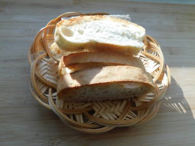 Hasır tabaktaki ekmeği kopyalanmış ahşap masada dilimler.
