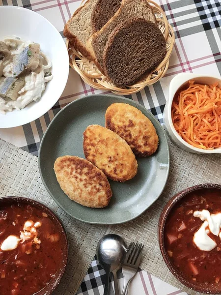 traditional Russian lunch, borscht, cutlets, fresh salad and black bread on the table.