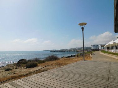 Yürüyen tahta patika deniz kenarında, mavi gökyüzü ve kuru sazlıklar. Protaras. Kıbrıs. Nisan 2021.