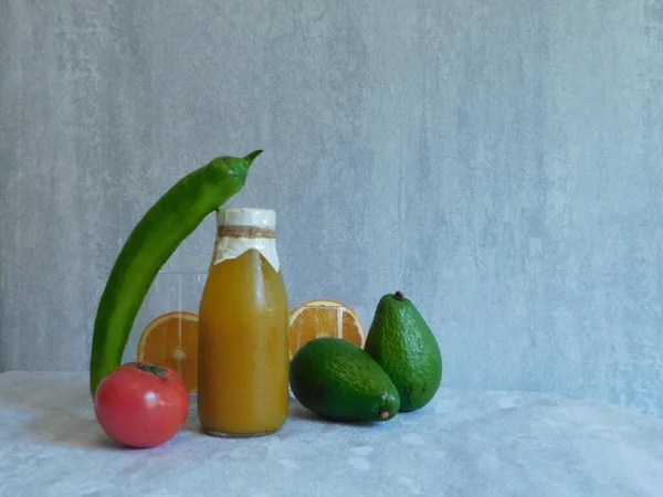 a bottle of orange juice, avocado, green long pepper, and half an orange on the table. free space for text. backgrounds and textures.