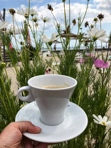 Een kopje koffie in een vrouwenhand op een achtergrond van bloemen. lucht en zee — Stockfoto