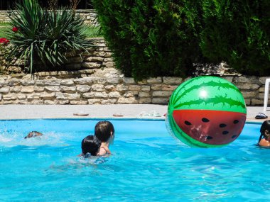 Karpuz şeklinde şişme bir top ve havuzda çocuklar.