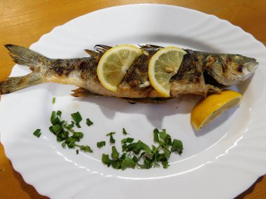 Tabakta limon dilimleri olan kızarmış levrek.
