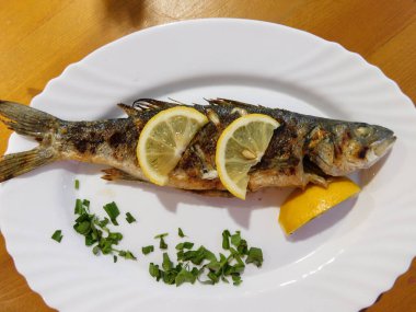 Tabakta limon dilimleri olan kızarmış levrek.