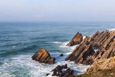 Atlantik kıyısındaki keskin kahverengi klipler ve mavi köpüklü okyanus ve ufuk manzarası.