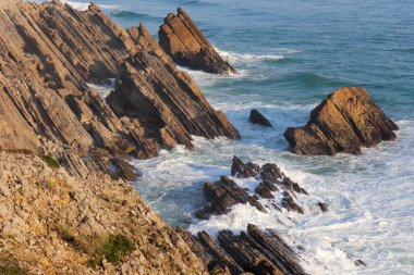 Atlantik kıyısındaki keskin kahverengi klipler ve mavi köpüklü okyanus ve ufuk manzarası.