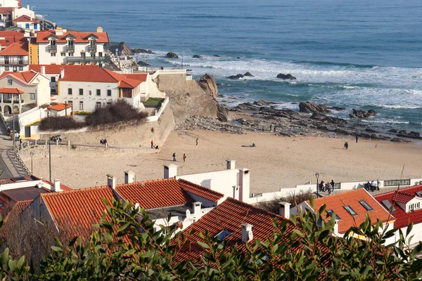 coastal village on the ocean from the bird\'s eye view directly on the beach and people with the view over green bushes down to the village and beach and the ocean to the horizon and blue, cloudless sky