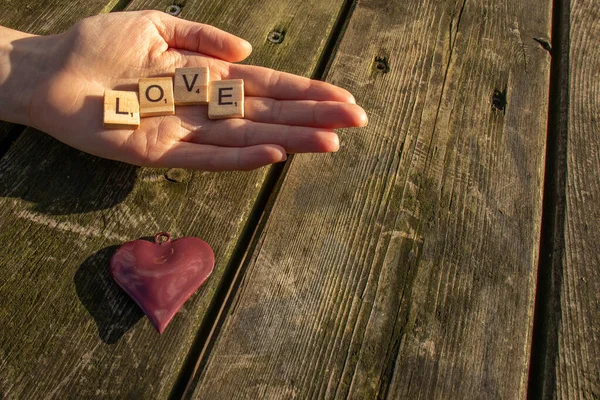 one woman hand with the letters love and a red heart with a dark wooden background