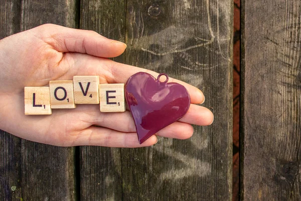 one woman hand with the letters love and a red heart with a dark wooden background