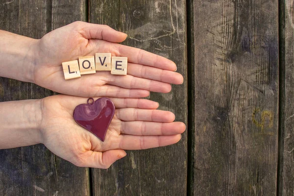 two woman hands with the letters love and a red heart with a dark wooden background