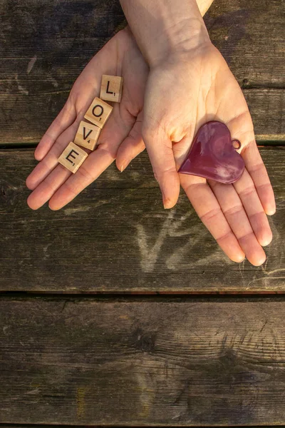 two woman hands with the letters love and a red heart with a dark wooden background