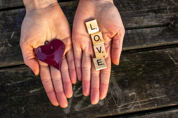 two woman hands with the letters love and a red heart with a dark wooden background