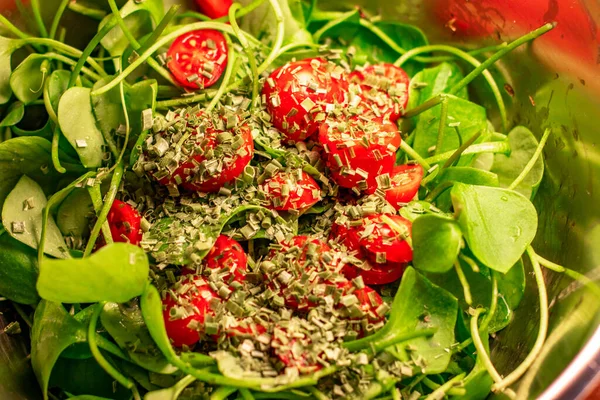 Küçük domateslerden yapılmış salata, kiraz domatesleri, yeşil geniş yapraklar ve metal kasede küçük kesilmiş kuru otlarla ince saplar.