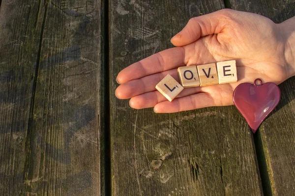 one woman hand with the letters love and a red heart with a dark wooden background