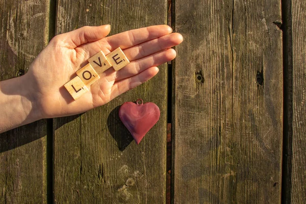 one woman hand with the letters love and a red heart with a dark wooden background