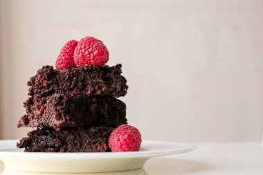 Stack of dark chocolate raspberry brownies on a white plate against light background with copy space