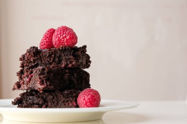 Stack of dark chocolate raspberry brownies on a white plate against light background with copy space clipart