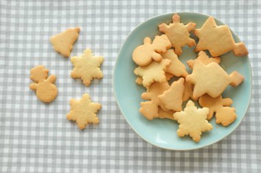 Beyaz ve gri karlı masa örtüsü üzerinde ev yapımı Noel kurabiyeleri (kardan adam, kar tanesi, zil).