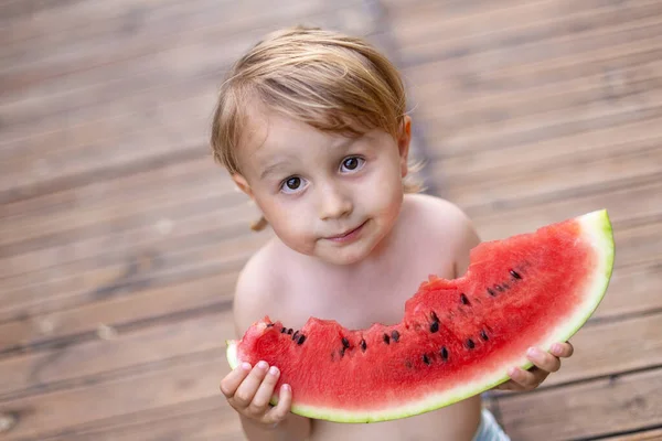 Child eating watermelon in the garden during summer vacances. Kids eat fruit outdoors. Healthy snack for children. Little boy tasting a slice of water melon.