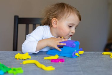 Küçük çocuk hamurla oynuyor, renkli modellik bileşimi evde ya da anaokulunda masada oturuyor. Çocuklarla yaratıcı eğlence..