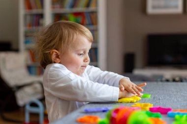 Mutlu gülümseyen küçük çocuk renkli kille tek başına oynuyor. Çocuk plasticin kullanıyor ve hamur oynuyor.