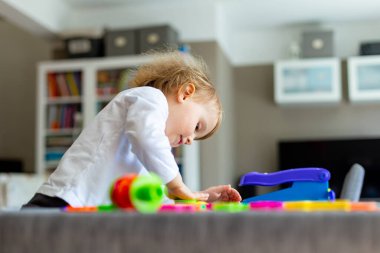 Küçük mutlu çocuk masada oturuyor ve renkli kil oyuncaklarla oynuyor. Koronavirüs karantinası sırasında evde plastikinden modellik yapan genç bir çocuk..