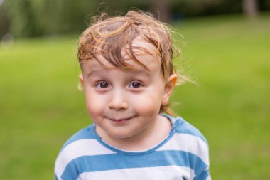 Parklarda gülümseyen küçük bir çocuğun portresini yakından çek. İki yaşında tatlı bir çocuk. Sıcak yaz havasında terli saçları var..