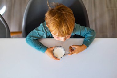 Süt ya da yoğurt içen ve karamel yiyen sevimli küçük çocuk sabahları mutfakta kahvaltı yapıyor.
