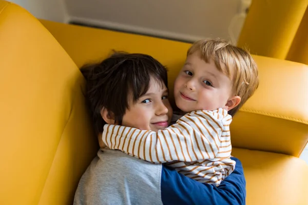 Δύο Αδέλφια Αγκαλιάζονται Και Αγκαλιάζονται Καθισμένοι Κίτρινο Καναπέ Εσωτερικούς Χώρους — Φωτογραφία Αρχείου