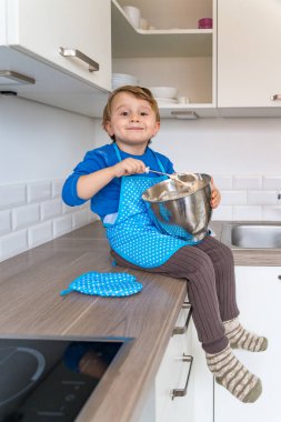 Küçük çocuk mutfak önlüğü giyip elmalı turta pişiriyor. Mutlu çocuk evde pasta ve mikserle oynuyor ve çalışıyor. Çocuk yemek pişirmede annesine yardım ediyor.