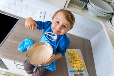 Mutfak önlüğü giymiş, elmalı turta pişiren güzel, komik, küçük bir çocuk. Mutlu çocuk evde pasta ve mikserle oynuyor ve çalışıyor. Çocuk pasta tadıyor.