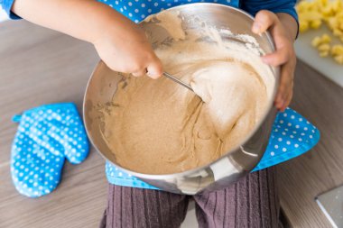 Mutfak önlüğü giymiş, elmalı turta pişiren güzel, komik, küçük bir çocuk. Mutlu çocuk evde pasta ve mikserle oynuyor ve çalışıyor. Annesine yardım eden çocuk