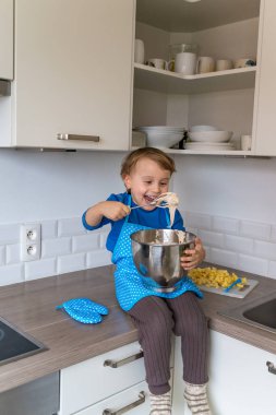 Güzel, komik bir çocuk kek pişiriyor ve ev mutfağında hamur tadıyor. Mutlu çocuk evde meyve ve hamur işleriyle eğleniyor ve çalışıyor..