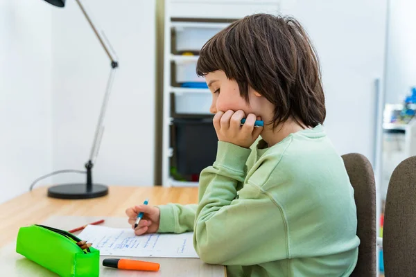 少年は宿題をして家のテーブルに座っている 集中力のある子供が課題を考えます ホームスクーロン教育 — ストック写真