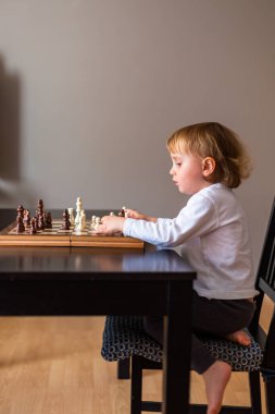 Küçük çocuk satranç oynamayı öğrendi. Evdeki masada oturan çocuk satranç tahtasının yanında. Erken satranç eğitimi.