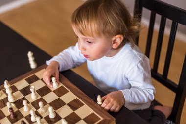 Küçük çocuk satranç oynamayı öğrendi. Evdeki masada oturan çocuk satranç tahtasının yanında. Erken satranç eğitimi.