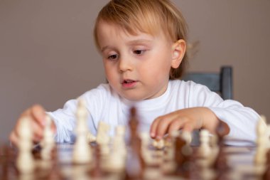 Küçük çocuk satranç oynamayı öğrendi. Evdeki masada oturan çocuk satranç tahtasının yanında. Erken satranç eğitimi.