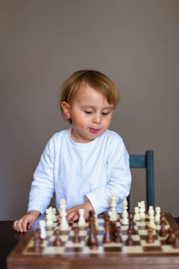 Küçük çocuk satranç oynamayı öğrendi. Evdeki masada oturan çocuk satranç tahtasının yanında. Erken satranç eğitimi.