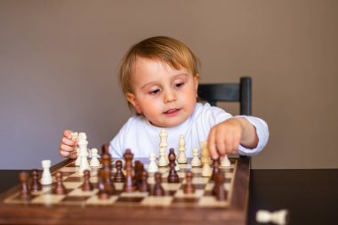 Küçük çocuk satranç oynamayı öğrendi. Evdeki masada oturan çocuk satranç tahtasının yanında. Erken satranç dersi.