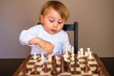 Küçük çocuk satranç oynamayı öğrendi. Evdeki masada oturan çocuk satranç tahtasının yanında. Erken satranç dersi.