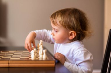 Küçük çocuk satranç oynamayı öğreniyor. Evdeki masada oturan çocuk satranç tahtasının yanında. Erken gelişim. Okul öncesi eğitim kavramı.