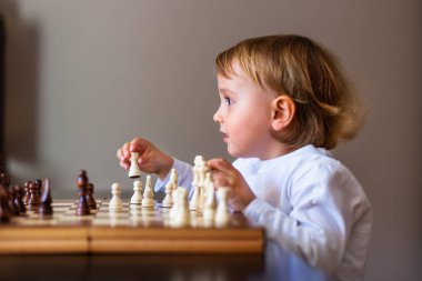 Küçük çocuk satranç oynamayı öğreniyor. Evdeki masada oturan çocuk satranç tahtasının yanında. Erken gelişim. Okul öncesi eğitim kavramı.