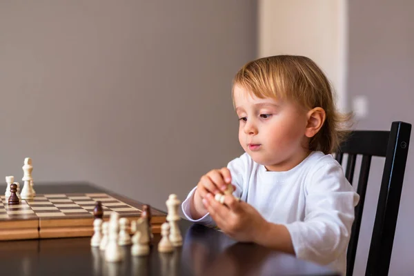 Little toddler boy learn to play chess. Child sitting at the table at home near the chessboard. Early chess education.