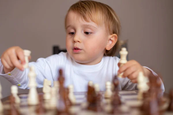 Little toddler boy learn to play chess. Child sitting at the table at home near the chessboard. Early chess education.
