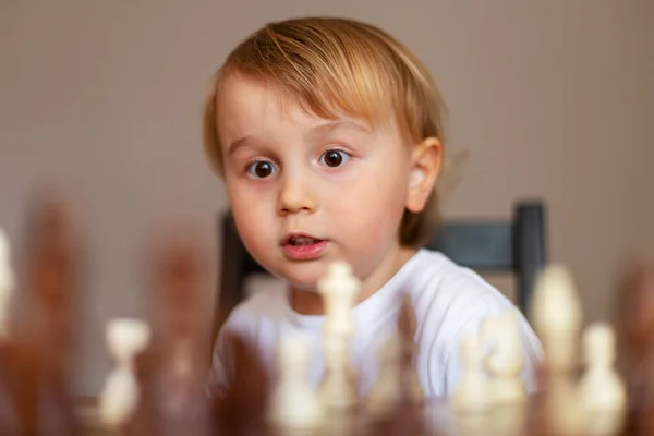 Little toddler boy learn to play chess. Child sitting at the table at home near the chessboard. Early chess education.