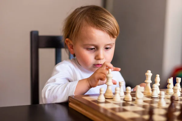 Menino fofo de 5 anos jogando xadrez sozinho em seu quarto em casa