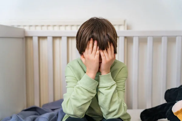 stock image Close up portrait of a young boy of ten years old sitting alone at home and crying. Upset depressed child closing face by hands.