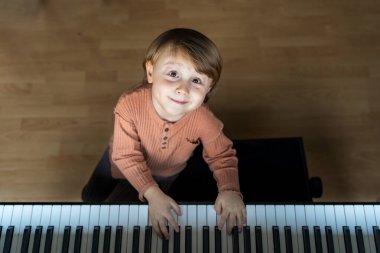 Küçük sevimli bir çocuğun portresi. Evde piyano çalan gülümseyen bir çocuk. Çocuk müzik öğreniyor. Erken gelişme.